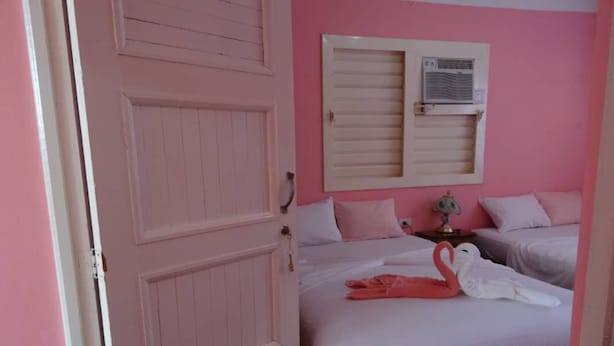 Quarto com decoração em tons de rosa, duas camas, um guarda-roupa e um ar condicionado fixado na parede.