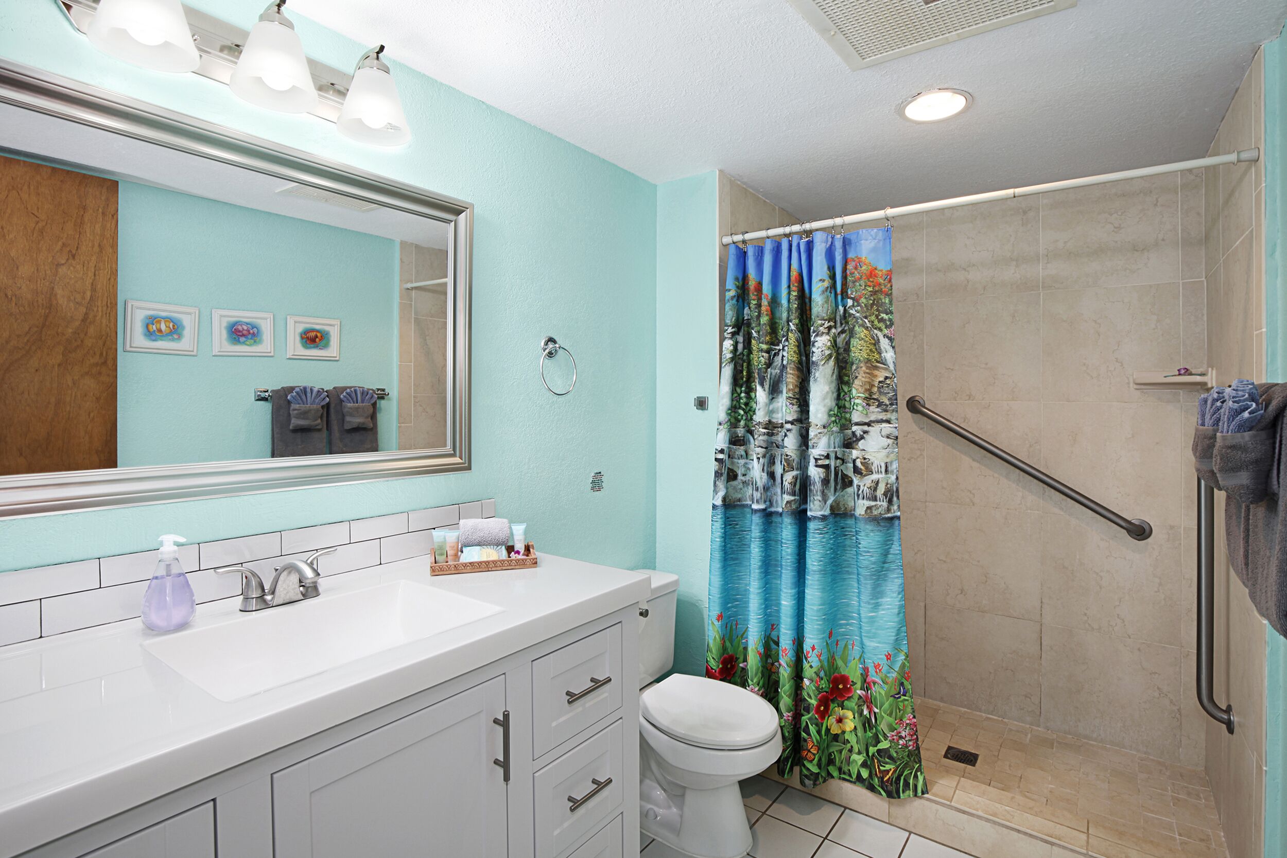 Ein Badezimmer mit Waschbecken, Spiegel, Toilette und Dusche mit blauer Duschvorhang.