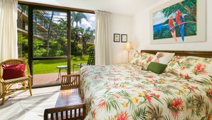 Ein Hotelzimmer mit Bett, Sessel, Tisch und Blick auf Garten und Gebäude durch ein großes Fenster.