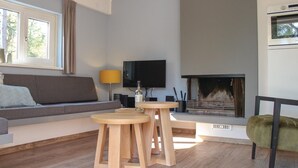 A modern living room with a fireplace, a sofa, a TV, and two wooden stools. - Cozy home in Ommen with sauna (Ommen)