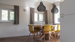 A dining area with a wooden table, four yellow chairs, two black hanging lights, and a window with curtains. - Cozy home in Ommen with sauna (Ommen)