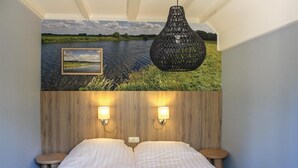 A bedroom with a bed, two wall-mounted lamps, a hanging light fixture, and a mural of a river scene. - Cozy home in Ommen with sauna (Ommen)