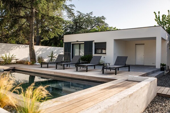 Una casa moderna con piscina, mobiliario de exterior y un jardín bien cuidado.