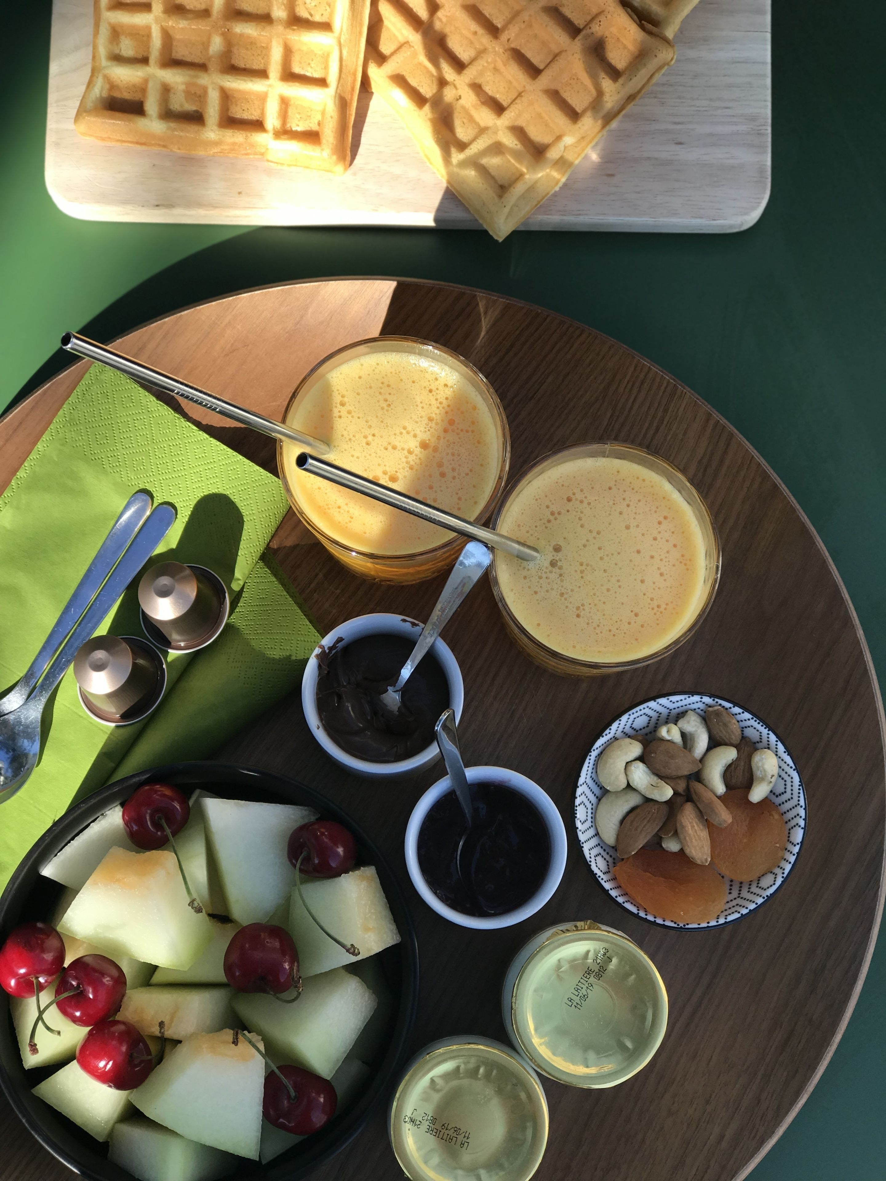 Un plateau de petit-déjeuner comprenant des gaufres, des fruits, des noix et deux types de boissons.