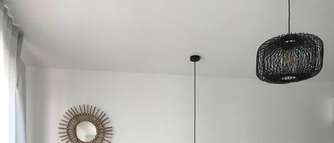 A modern bedroom with a bed, a round wooden side table, two wall-mounted light fixtures, and a woven rug.