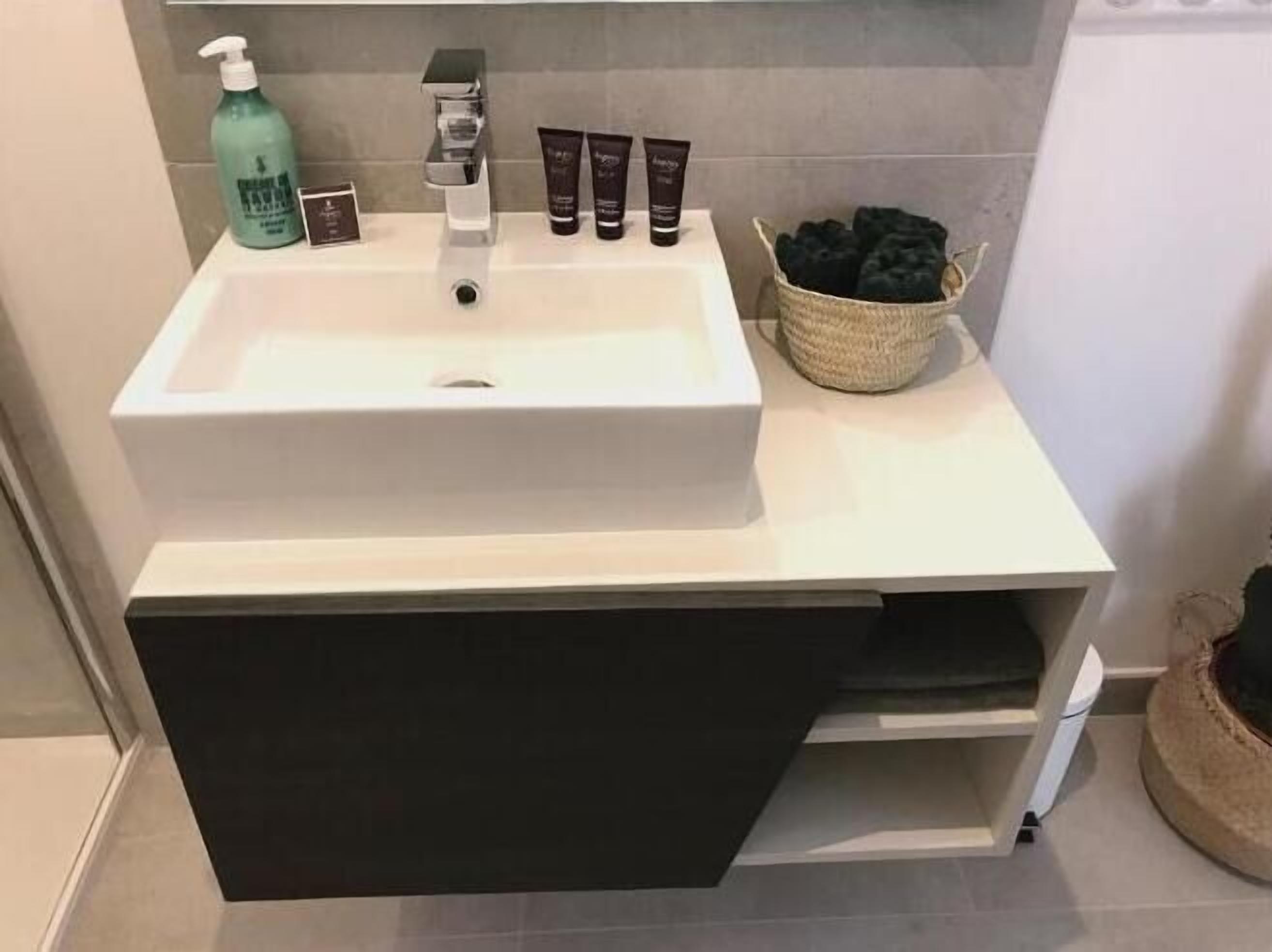 A bathroom with a white sink, a bottle of hand soap, and a basket of black towels.