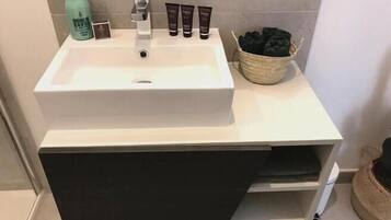A bathroom with a white sink, a bottle of hand soap, and a basket of black towels.