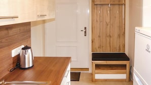 Una cocina compacta con encimera de madera, hervidor de acero inoxidable, refrigerador blanco y un banco de madera.
