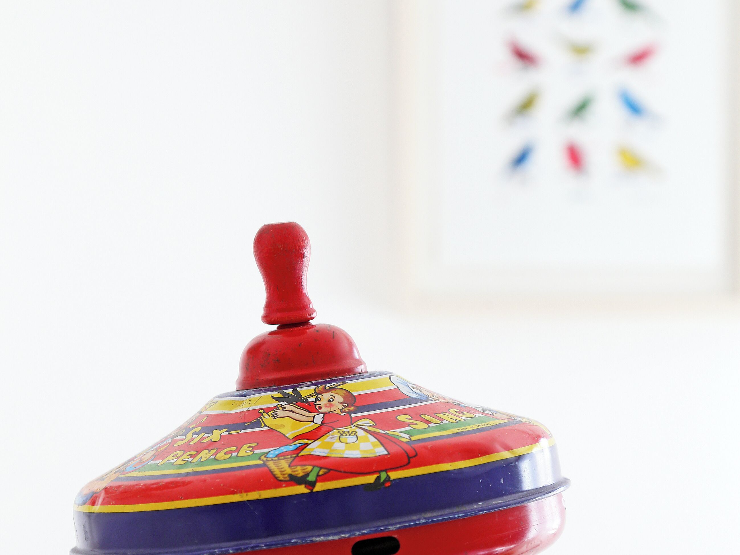 A vintage toy with a red handle and colorful illustrations on its lid.