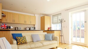 A modern living room with a sofa, a coffee table, and a dining area with wooden cabinets and a kitchen counter. - 2 bedroom accommodation in Whitstable (Whitstable)