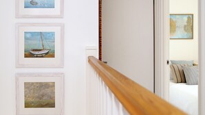 A hallway with three framed paintings of boats and birds, a wooden railing, and a glimpse of a bedroom with a bed and pillows. - 2 bedroom accommodation in Whitstable (Whitstable)