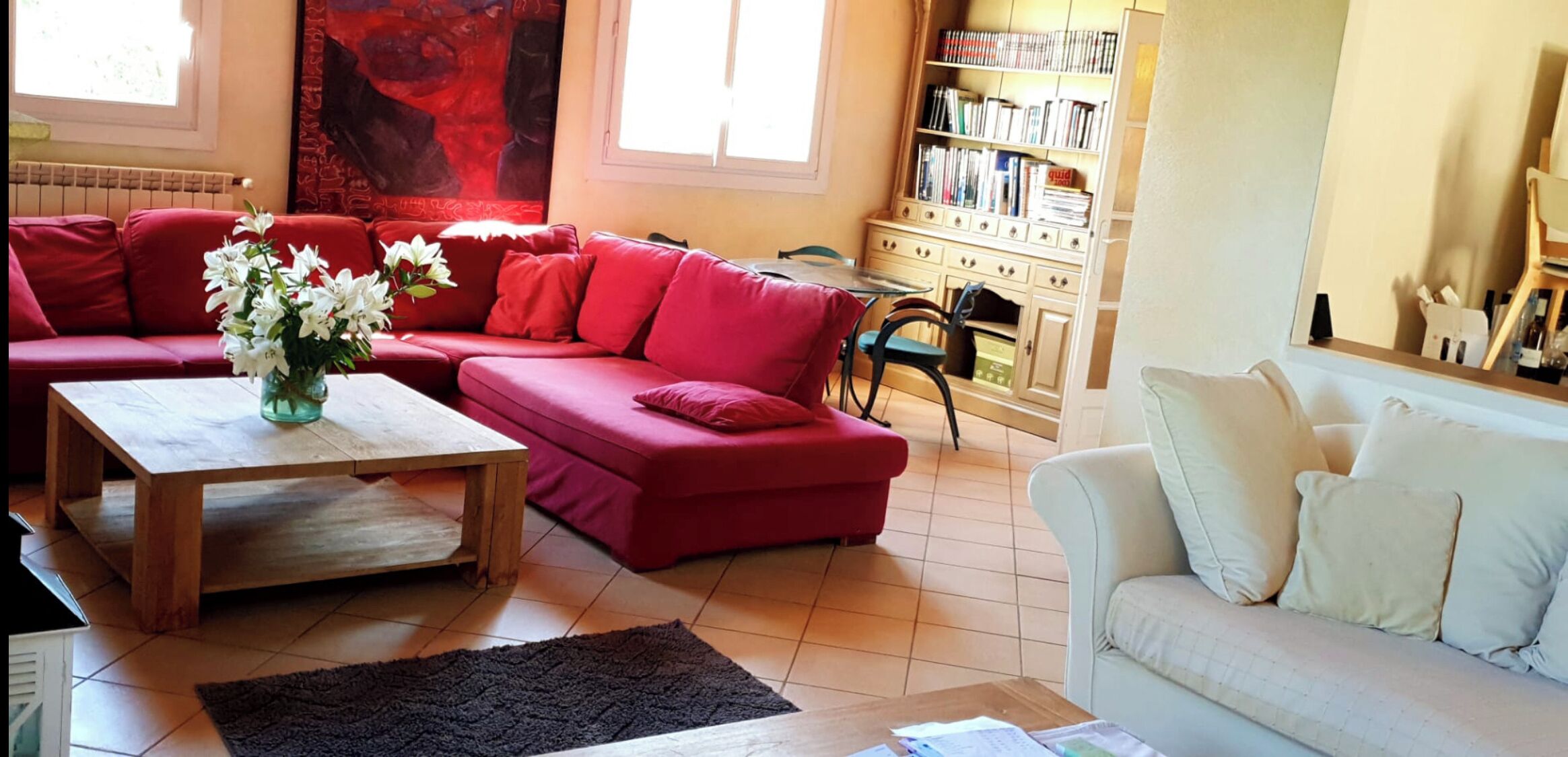 Una sala de estar con un sofá rojo, un sofá blanco, una mesa de centro de madera y una estantería llena de libros.