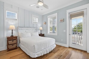 Une chambre avec un grand lit, deux tables de chevet avec des lampes, un ventilateur de plafond et une vue sur l’extérieur par une porte.