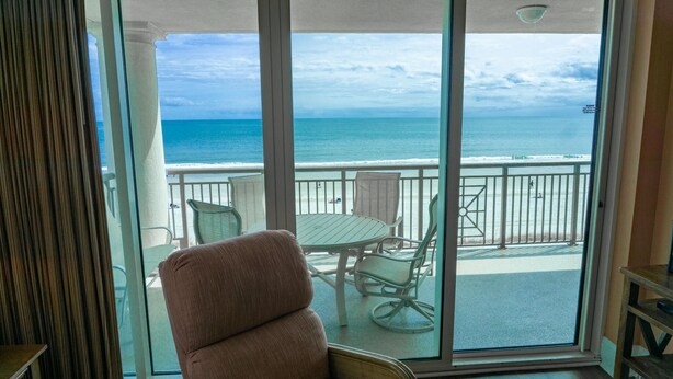 A balcony with a view of the ocean, a table, and a cushioned chair. - MVG 504 3 BEDROOM 3 BATH OCEANFRONT CORNER (North Myrtle Beach)