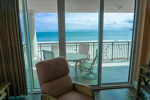 Un balcon avec vue sur l’océan, une table et un fauteuil rembourré.