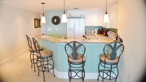Una cocina con una isla central, taburetes de bar, un refrigerador e iluminación colgante.