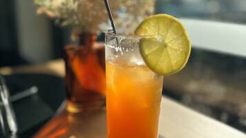 Un bicchiere alto con una cannuccia, contenente una bevanda, guarnito con una fetta di lime, su un tavolo con un cucchiaio e un vaso di fiori secchi sullo sfondo.