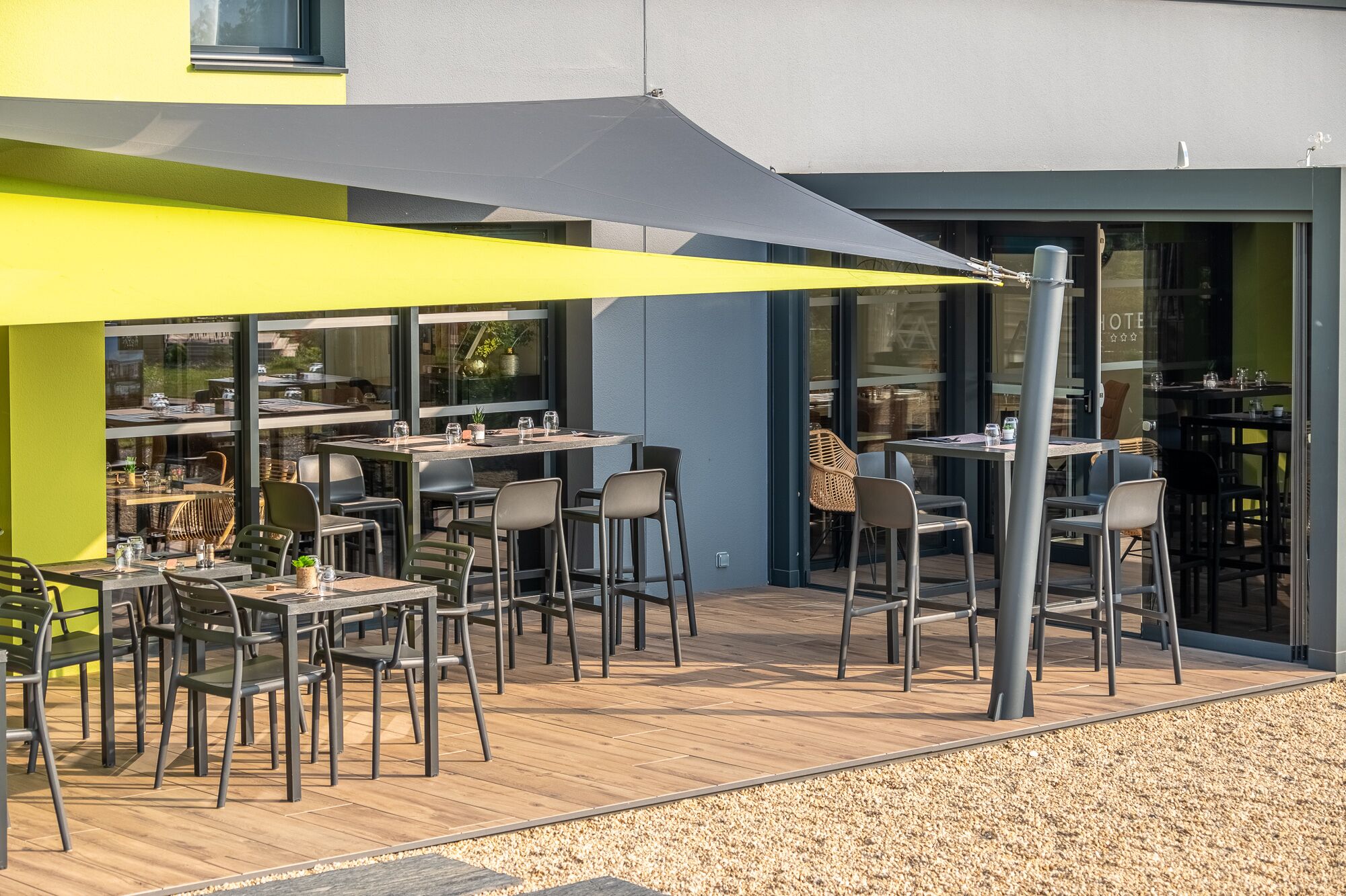 An outdoor dining area with tables and chairs, a large umbrella, and a building with glass doors in the background.