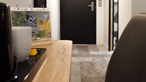 Ein Hotel-Empfangsbereich mit einem Holztresen, einer Kaffeemaschine, einem gerahmten Bild und einer schwarzen Tür am Ende des Flurs.