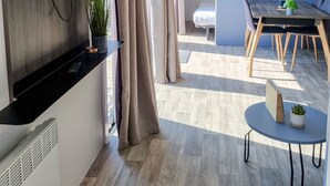 Ein modernes Wohnzimmer mit Flachbildfernseher, einem Essbereich mit Holztisch und Stühlen sowie einem kleinen runden Tisch mit Pflanze.