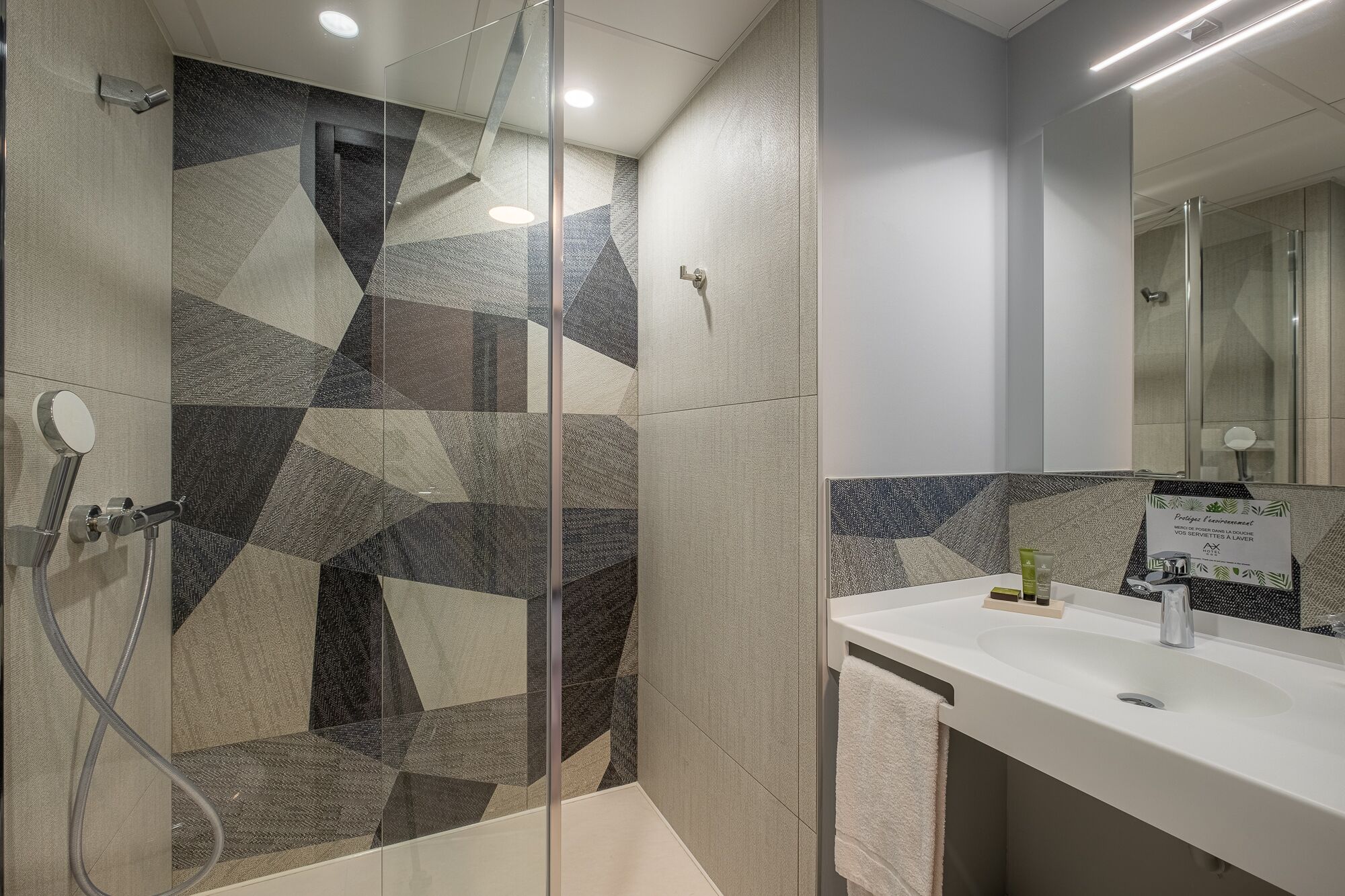 A modern bathroom with a shower area featuring geometric tile patterns, a white sink with toiletries, and a mirror above the sink.