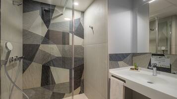 A modern bathroom with a shower area featuring geometric tile patterns, a white sink with toiletries, and a mirror above the sink.