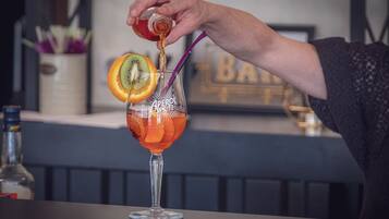 Un cantinero sirve una bebida en un vaso con pajita, decorada con una rodaja de naranja y un kiwi.