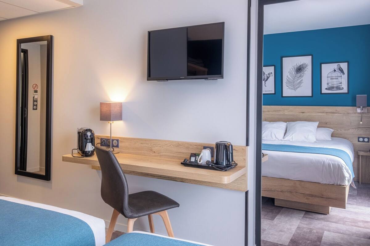 Une chambre d’hôtel équipée d’un bureau, d’une chaise, d’un lit, d’une télévision et d’œuvres d’art accrochées au mur.