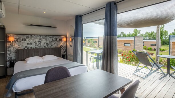 Ein modernes Hotelzimmer mit einem großen Bett, einem Schreibtisch und einem Balkon mit Sitzgelegenheit.