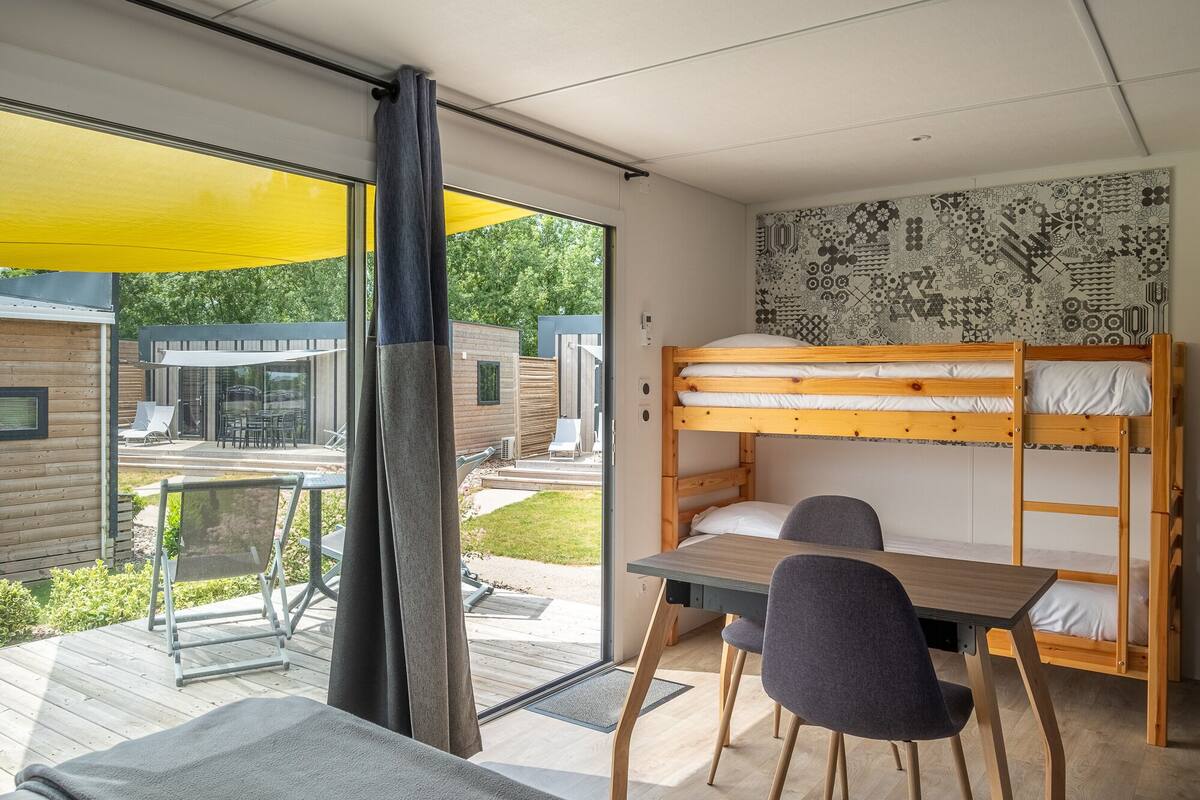 Une chambre moderne et compacte, équipée d’un lit superposé, d’une petite table et d’une chaise.