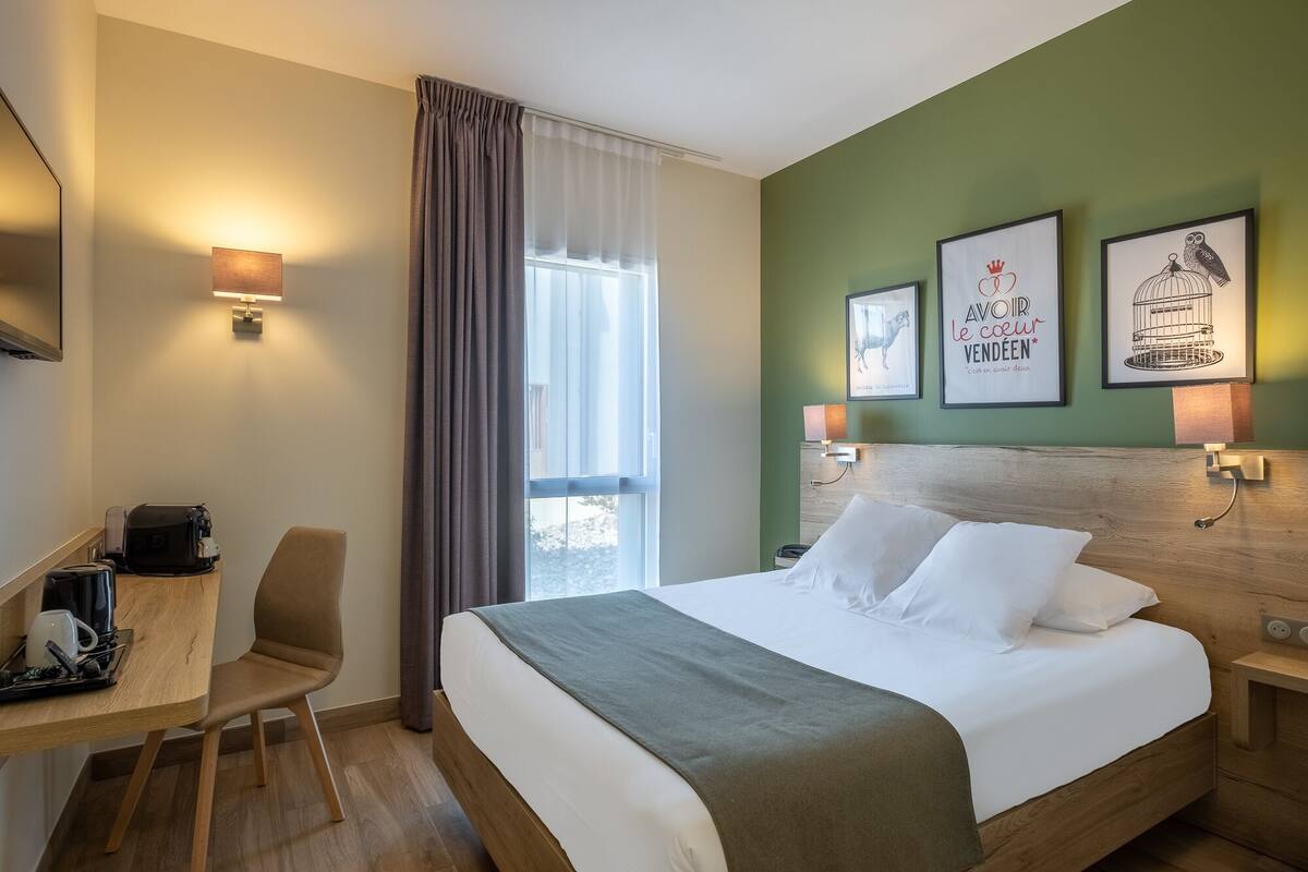Une chambre d’hôtel avec un lit, un bureau, une chaise et une fenêtre avec des rideaux.
