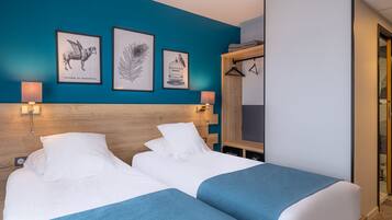 A hotel room with two beds, a wooden headboard, and wall art including a peacock feather and a peahen.