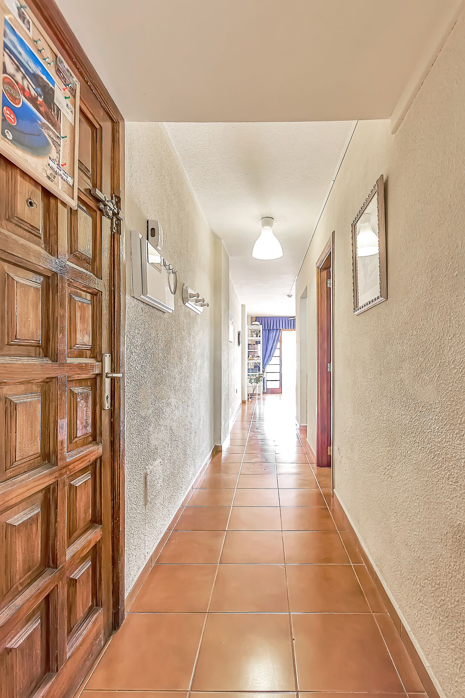 Un pasillo con puerta de madera, suelo de baldosas y una lámpara.