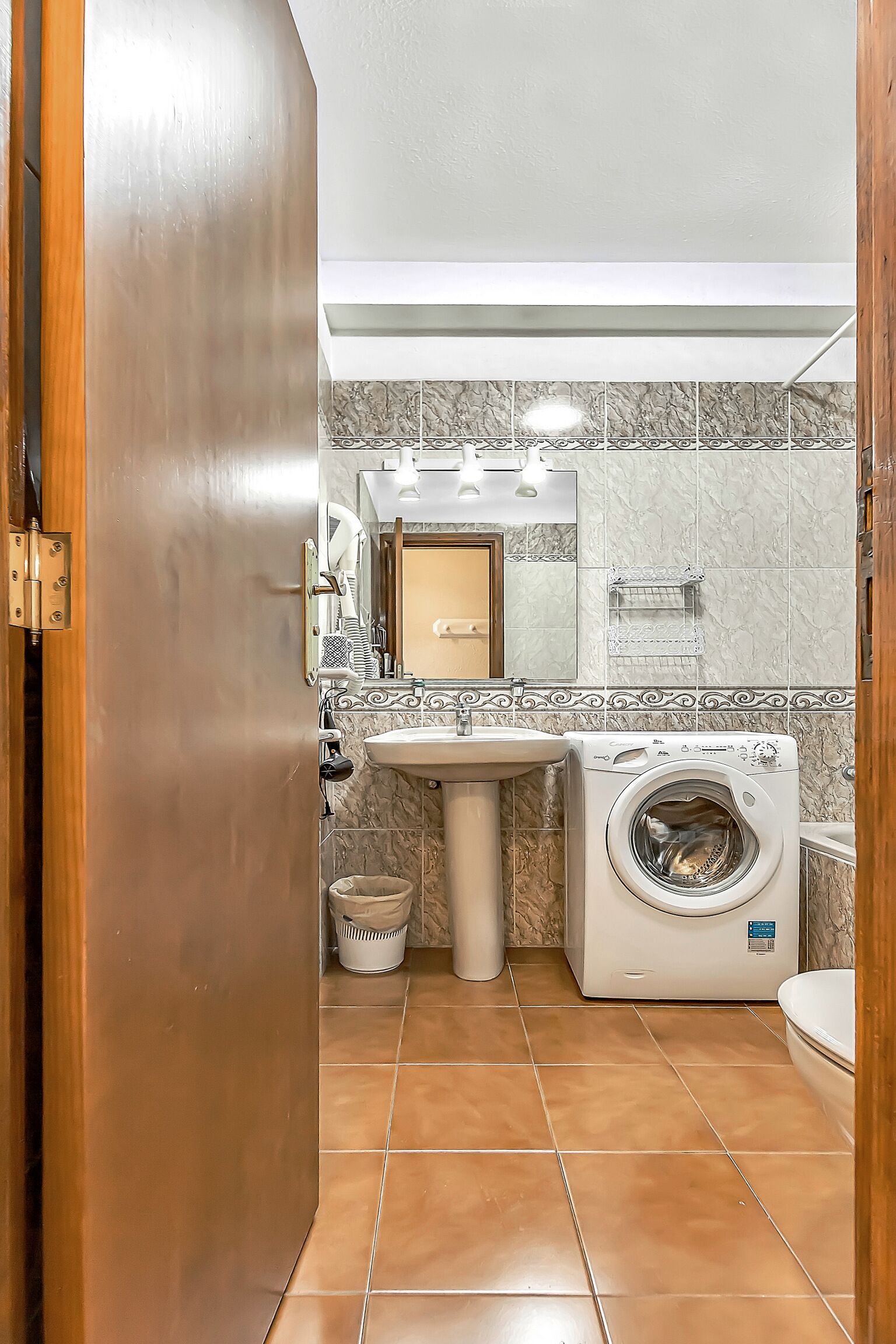 A compact bathroom with a washing machine, sink, and a mirror.