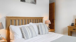 A neatly made bed with white bedding and striped pillows, a wooden headboard, and bedside tables with lamps and a small decorative item. - 1 bedroom accommodation in Near Woolsery (Near Woolsery)