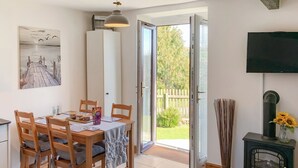 A dining area with a wooden table and chairs, a painting on the wall, and a view of the outdoors through an open door. - 1 bedroom accommodation in Near Woolsery (Near Woolsery)