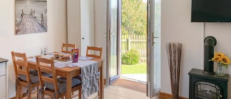 A dining area with a wooden table and chairs, a painting on the wall, and a view of the outdoors through an open door.