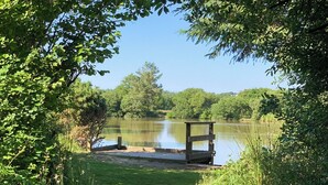 A wooden dock extending into a calm lake surrounded by dense greenery. - 1 bedroom accommodation in Near Woolsery (Near Woolsery)