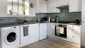 A compact kitchen with white cabinets, a built-in washing machine, a microwave, and a stove. - 1 bedroom accommodation in Near Woolsery (Near Woolsery)