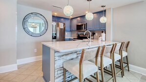 A modern kitchen with a central island, bar stools, pendant lighting, and a round mirror on the wall. - MVG 1404 Oceanfront Corner Penthouse (North Myrtle Beach)