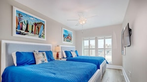 A hotel room with two beds, a ceiling fan, artwork on the walls, a window with a view, and a TV mounted on the wall. - MVG 1404 Oceanfront Corner Penthouse (North Myrtle Beach)
