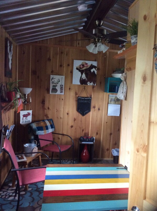 L’intérieur chaleureux d’un chalet avec des murs en bois, un ventilateur de plafond, une couverture à carreaux et un décor rustique comprenant un tableau représentant une vache et une pancarte de bienvenue.