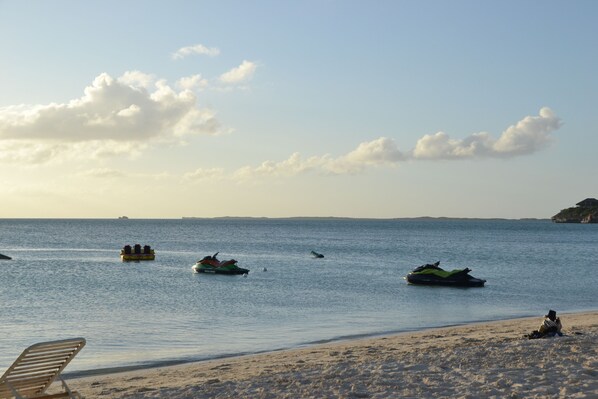 Uma praia com um jet ski, um barco e uma espreguiçadeira.