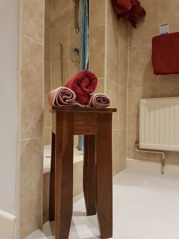 A wooden stool with rolled towels in a bathroom with beige tiles and a white radiator. - Milton's Country Lodge (Bristol)