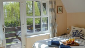A bedroom with a bed, a breakfast tray with croissants, juice, and fruit, and a view of greenery through the window. - 3 bedroom accommodation in Cromer (Cromer)