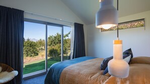 A bedroom with a large bed, a view of the outdoors, and a modern pendant light. - The Arrow Nest - Beautiful Stylish Apartment (Arrowtown)