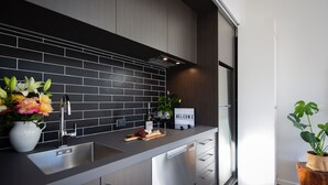 A modern kitchen with a black tiled backsplash, stainless steel appliances, and a welcome sign. - The Arrow Nest - Beautiful Stylish Apartment (Arrowtown)
