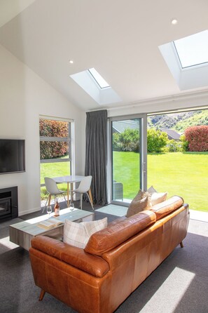 A modern living room with a leather sofa, a flat-screen TV, and a dining area with a table and chairs. - The Arrow Nest - Beautiful Stylish Apartment (Arrowtown)