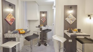 A modern kitchen with two bar stools, a dining table, and a breakfast setup with orange juice and a bowl of fruit. - Better & Better (Palermo)
