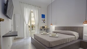 A modern bedroom with a large bed, a TV mounted on the wall, a desk with a lamp, and a view of the outdoors through a window. - Better & Better (Palermo)